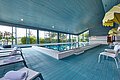 Ein großer Indoor Pool mit blauen Fliesen und Liegestühlen mit Sonnenschirmen.