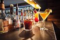 Drei Cocktails sind auf dem schwarzen Tresen platziert, im Hintergrund befindet sich eine Bar.