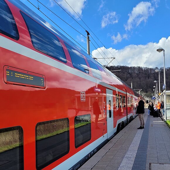 Eine Regionalbahn hat am Gleis gehalten und Reisende warten darauf, dass sich die Türen öffnen.