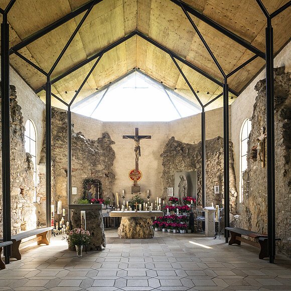 Ruinenkirche Spindeltal Innenraum einer Kapelle mit Altar, Kreuz, Kerzen und Blumen, umgeben von alten Steinmauern und Holzdecke