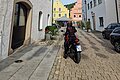 Motorradfahrer auf gepflasterter Straße mit bunten Lampions über Kopf und historischen Häusern.