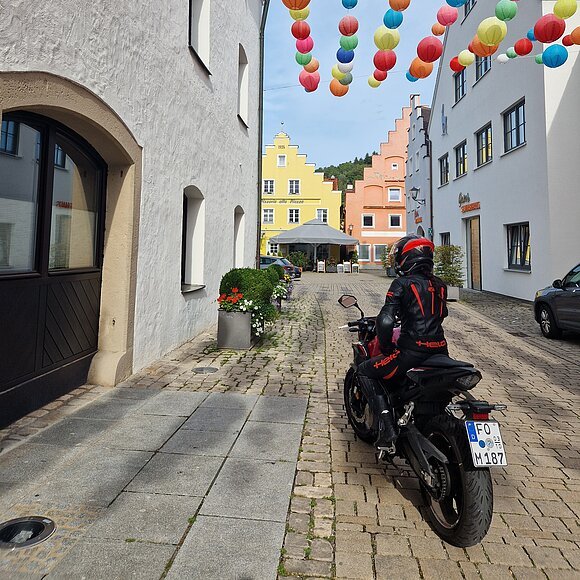 Motorradfahrerin in der Altstadt von Beilngries Motorradfahrer in schwarzer Schutzkleidung auf Kopfsteinpflasterstraße mit bunten Lampions und farbigen Häusern.
