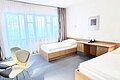 Doppelzimmer im ABG Tagungszentrum Hotelzimmer mit zwei Einzelbetten, Schreibtisch, zwei Stühlen und großen Fenstern mit Gardinen.