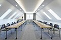 Konferenzraum mit zwei langen Tischen, Stühlen und Dachfenstern in einem hellen Raum mit Teppichboden.