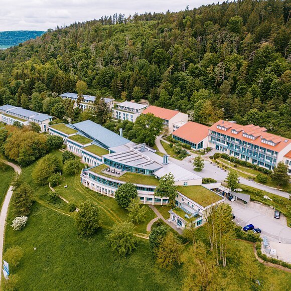 Tagungshaus AGB Beilngries Hauptbild Gebäude Luftaufnahme eines Gebäudekomplexes mit grünen Dächern am Waldrand und umliegenden Wiesen und Wegen.