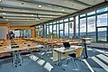 Foyer im ABG Tagungszentrum Großer Seminarraum mit Reihen von Tischen und Stühlen, Laptop auf vorderem Tisch, große Fenster mit Blick ins Freie.
