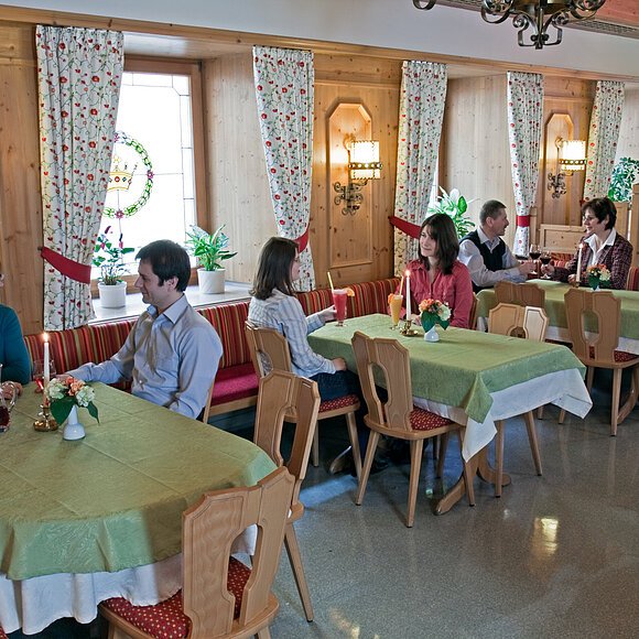 Gastraum mit Holzwänden, grünen Tischdecken, mehreren Gästen an Tischen und Kerzenlicht in einem Restaurant.