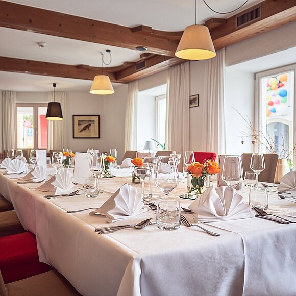 Veranstaltungsraum im Hotel Fuchsbräu Großer Esstisch mit weißer Tischdecke, gefalteten Servietten, Gläsern und Blumen in einem Raum mit Holzdecke.