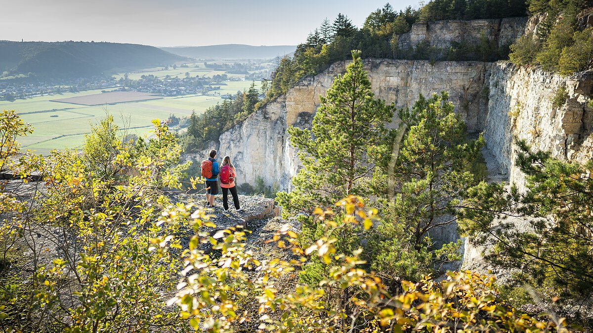 Zwei Personen mit Rucksäcken stehen auf einem Felsvorsprung und blicken ins Tal.