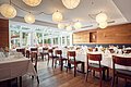 Restaurant mit gedeckten Tischen, Holzstühlen, großen Fenstern und runden Papierlampen an der Decke.