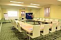 Tagungsraum mit U-förmiger Tischanordnung, weißen Stühlen, Flipchart und Projektor mit Leinwand.
