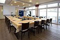 Konferenzraum mit U-förmiger Tischanordnung, Stühlen, Flipchart, Projektor und großen Fenstern mit Blick nach draußen.