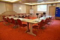 Konferenzraum mit U-förmiger Tischanordnung, Stühlen, Flipchart und Projektor mit Hotel-Logo-Beamerbild.